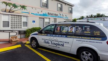 A white van parked in front of Richard's Hotel with a tropical mural on the wall.