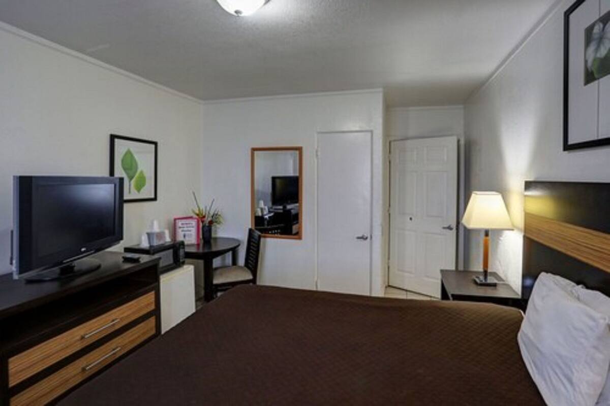 A hotel room with a bed, a TV, a desk with a chair, a lamp, and a door.