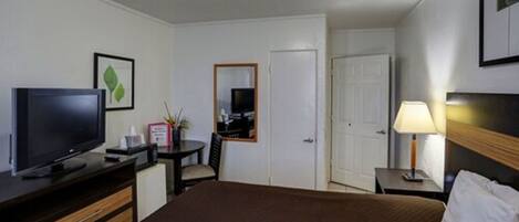 Une chambre d’hôtel avec un lit, une télévision, un bureau avec une chaise, une lampe et une porte.