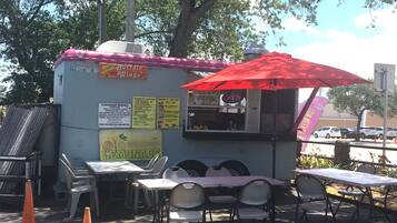 A food truck with a red umbrella, offering Canadian dishes and lemonade. Tables and chairs are set up for outdoor dining.