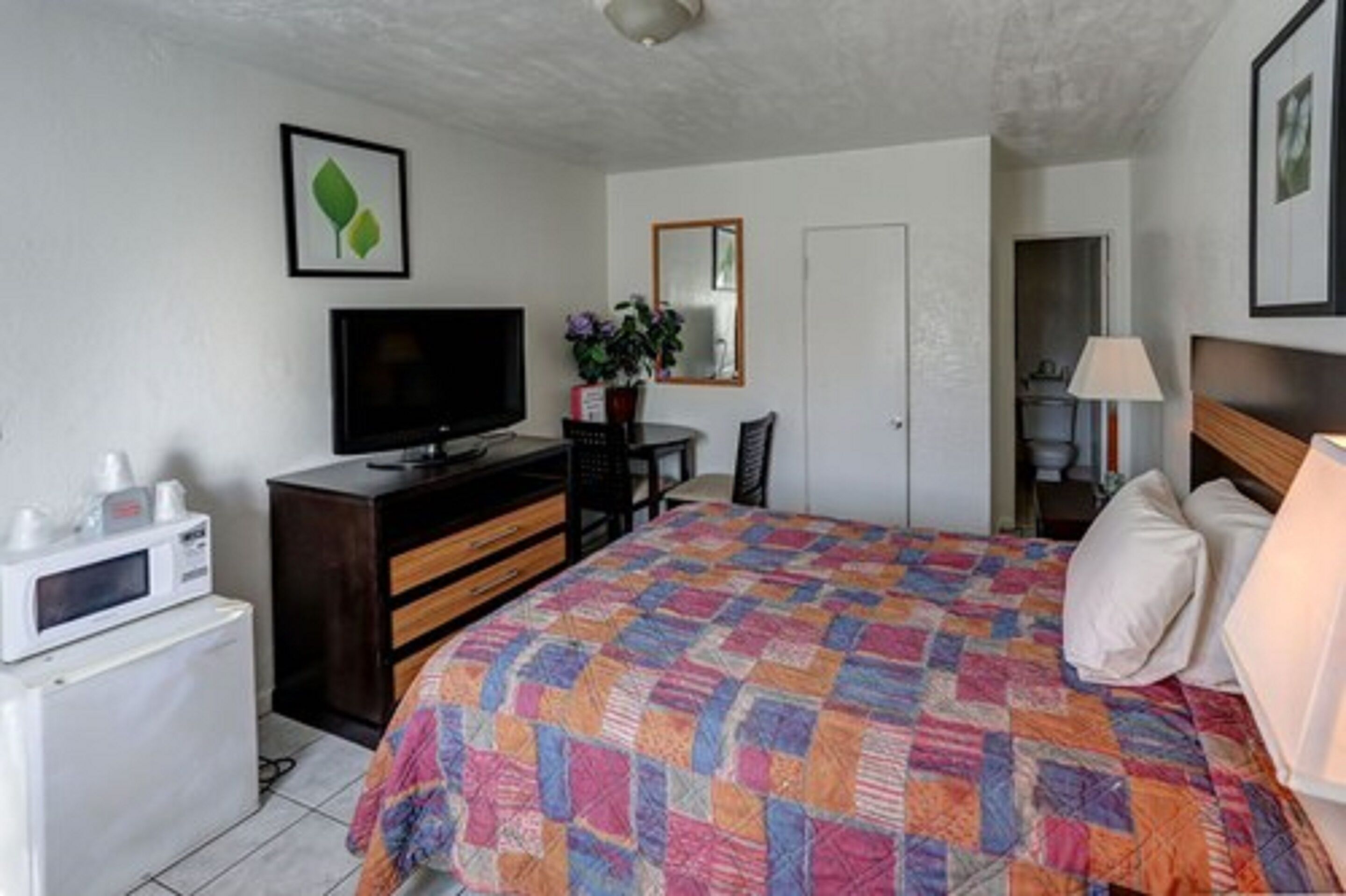 A hotel room with a bed, a television, a desk, a chair, a microwave, and a door leading to another room.