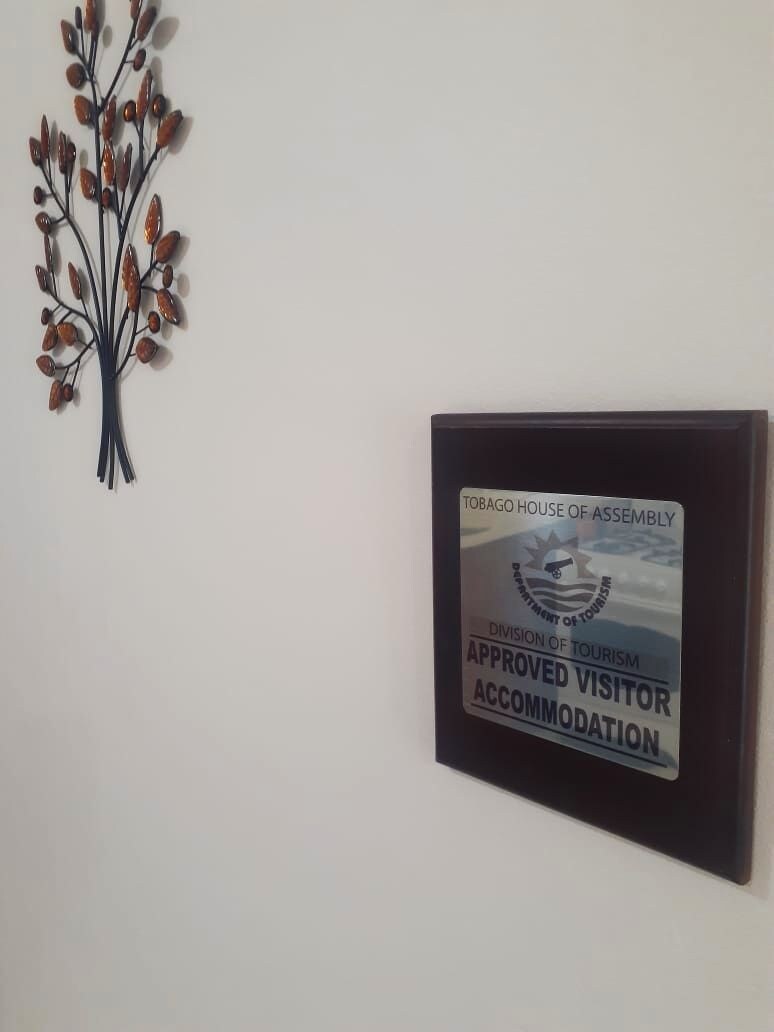 A wall-mounted plaque with a logo and text indicating it is an approved visitor accommodation by the Tobago House of Assembly.