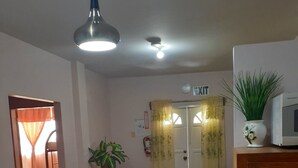 Une cuisine avec des meubles de rangement en bois, une table à manger avec des chaises, un luminaire au plafond et un four à micro-ondes posé sur un meuble.