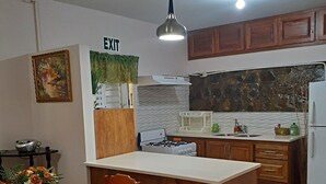 Une cuisine avec des meubles en bois, un plan de travail blanc, une cuisinière à gaz et un coin repas comprenant une table et des chaises.