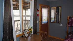Quarto com mesa de jantar de madeira, duas cadeiras, um banco de madeira, porta com espelho e janela com cortinas.