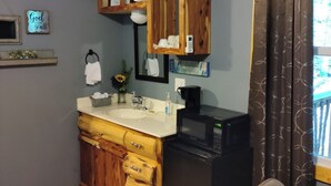 Uma cozinha compacta com armários de madeira, uma pia, micro-ondas e um espaço de refeições com mesa e cadeiras.