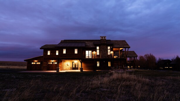A large, two-story wooden house with multiple windows and a well-lit front entrance. - New! Luxury Mountain Escape in Majestic Playground (Tetonia)