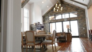 A spacious dining area with a high ceiling and exposed beams, a stone fireplace, and large windows allowing natural light. - New! Luxury Mountain Escape in Majestic Playground (Tetonia)