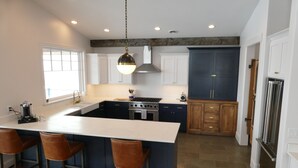 A modern kitchen with a central island, bar stools, a stainless steel refrigerator, and a large window. - New! Luxury Mountain Escape in Majestic Playground (Tetonia)