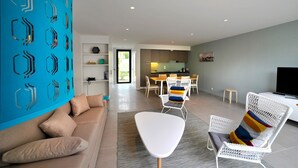 A modern living room with a sofa, a white chair with colorful cushions, and a dining area with a table and chairs. - Villa for 6 people 300m from the beaches for 6 people (La Palmyre)