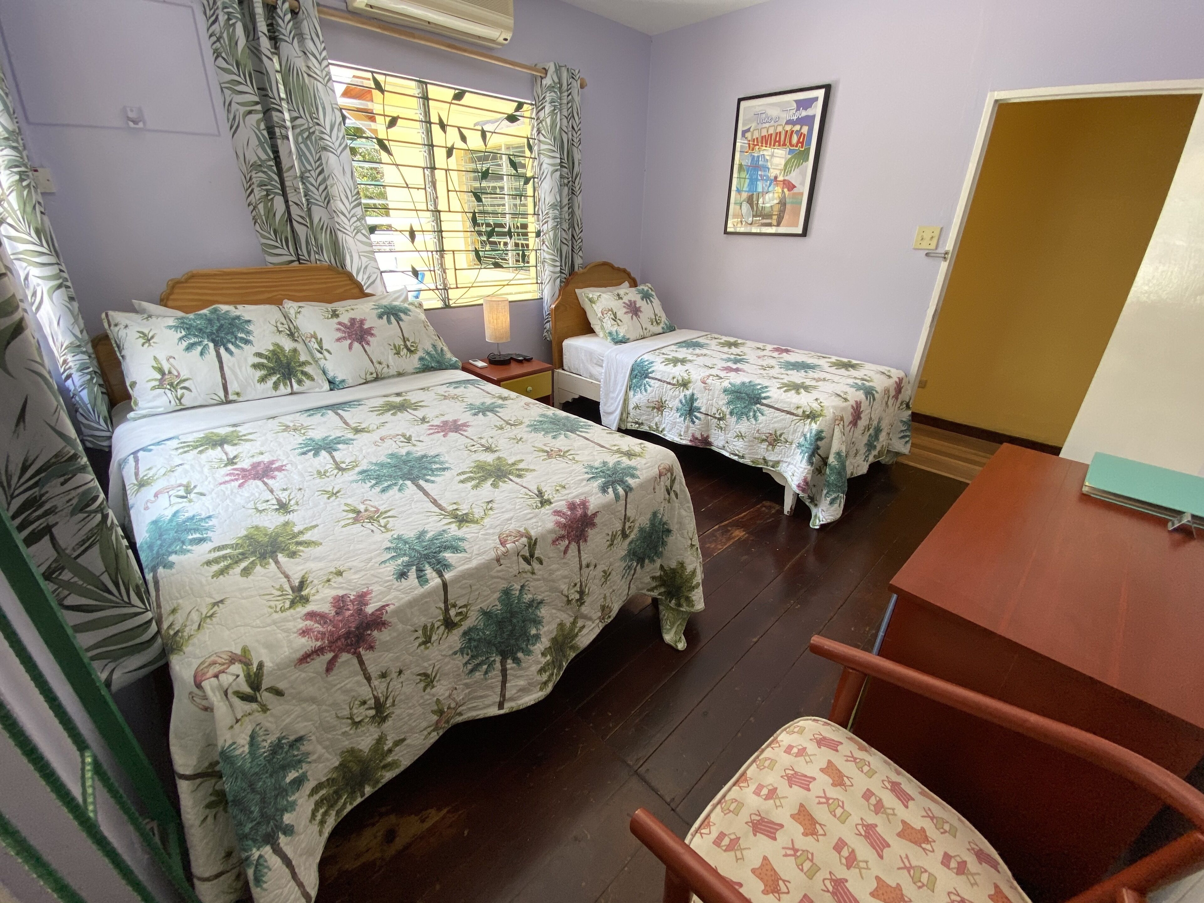 A room with two beds, a wooden chair, a table, and a window with curtains.