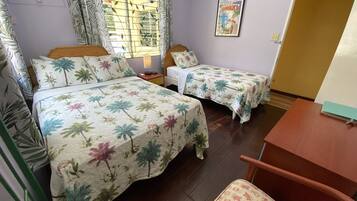 A room with two beds, a wooden chair, a table, and a window with curtains.