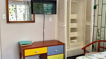 Un dormitorio con una cama, una mesita de noche, un espejo, un televisor y un armario.