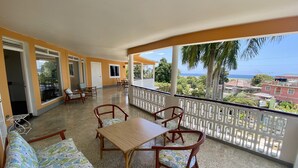 A balcony with a wooden table and chairs, a sofa, and a view of the ocean. - Palm Garden (Montego Bay)