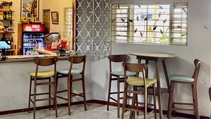 A café with wooden chairs and a tiled floor, a counter with a beverage cooler, and a window with a view of greenery. - Palm Garden (Montego Bay)