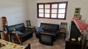 A living room with a sofa, chairs, a television, and a window with blinds. - 800 mts da Praia (SP)
