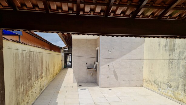 A covered outdoor area with tiled flooring, a concrete wall, and a metal roof structure. - 800 mts da Praia (SP)