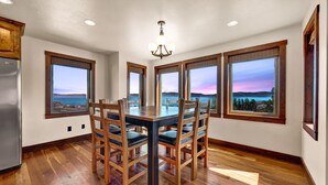 A dining room with a wooden table and chairs, large windows with a view of the landscape, and a chandelier.