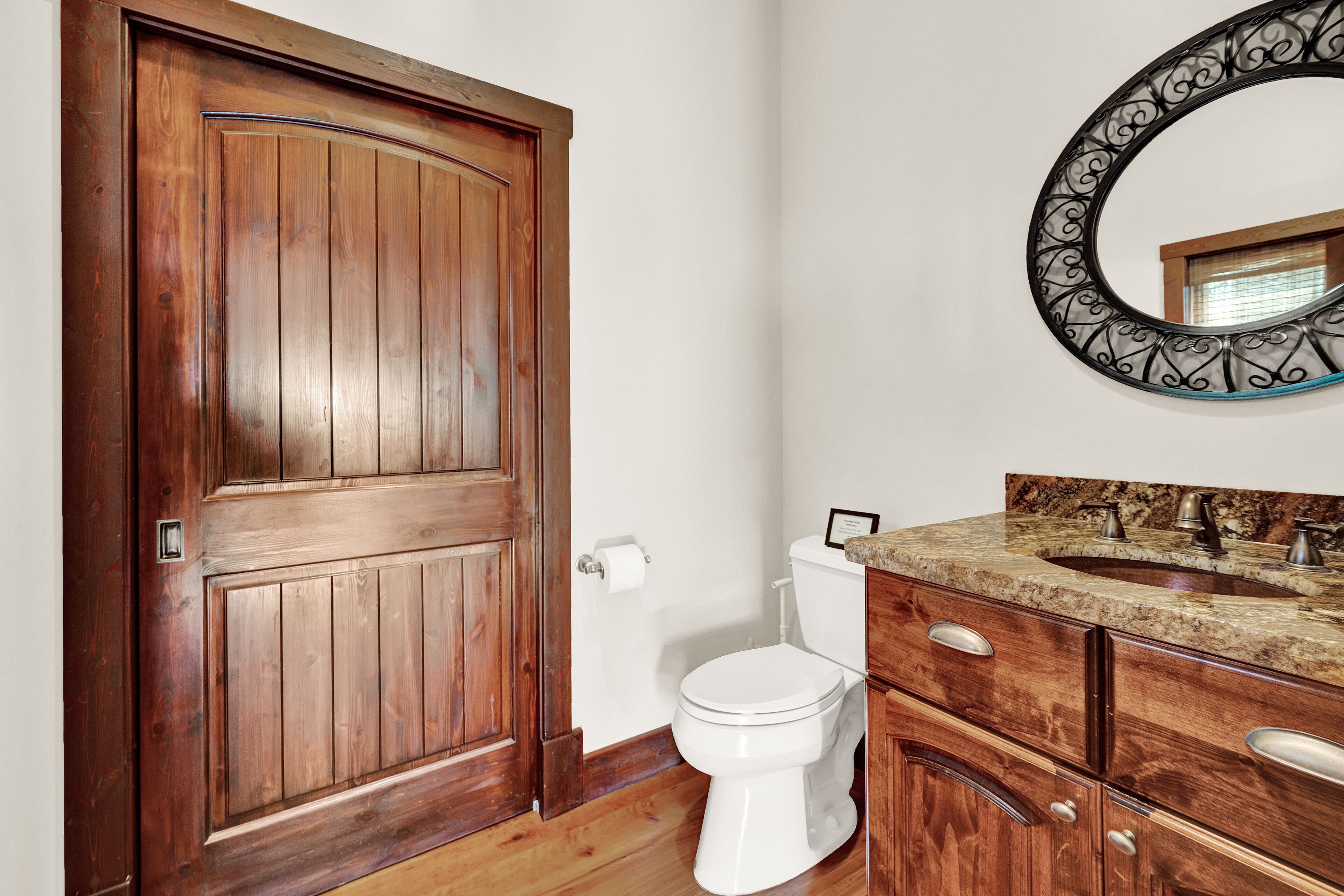 Una porta in legno, un water bianco, un mobile bagno con piano in marmo e uno specchio decorativo.