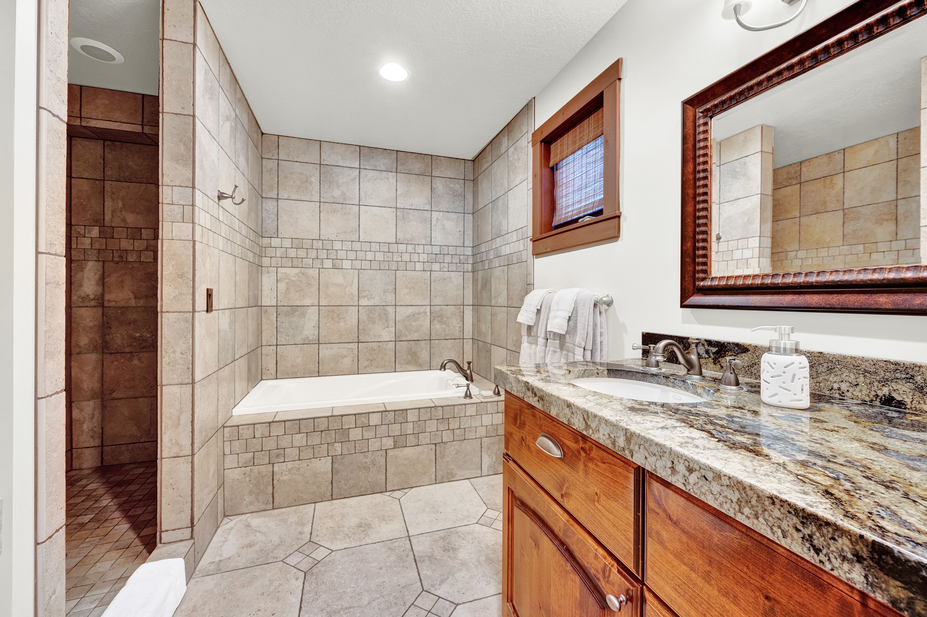 A bathroom with a bathtub, a sink, a mirror, and a shower area.