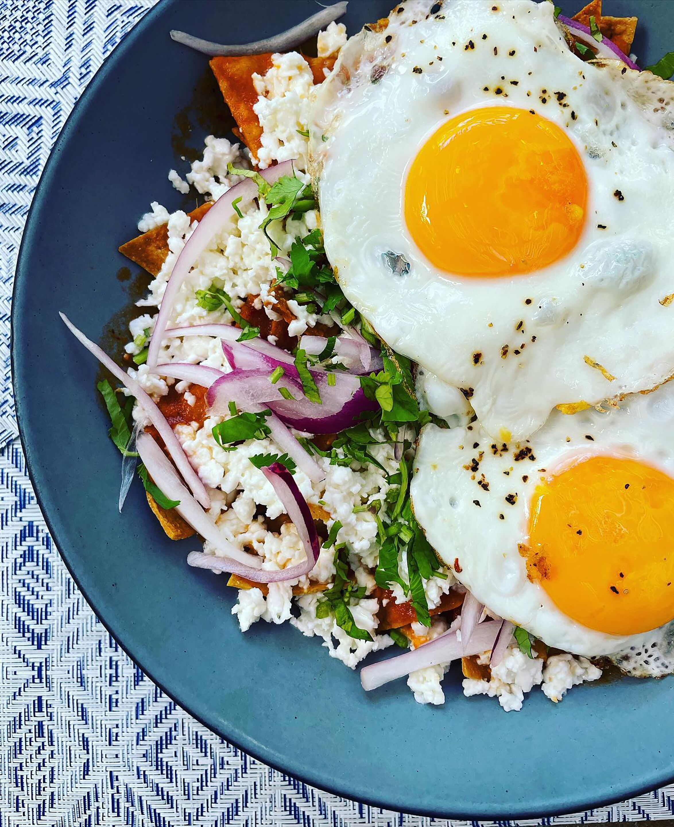 Un plato de comida con dos huevos fritos, cebollas rojas y una guarnición de hierbas verdes.