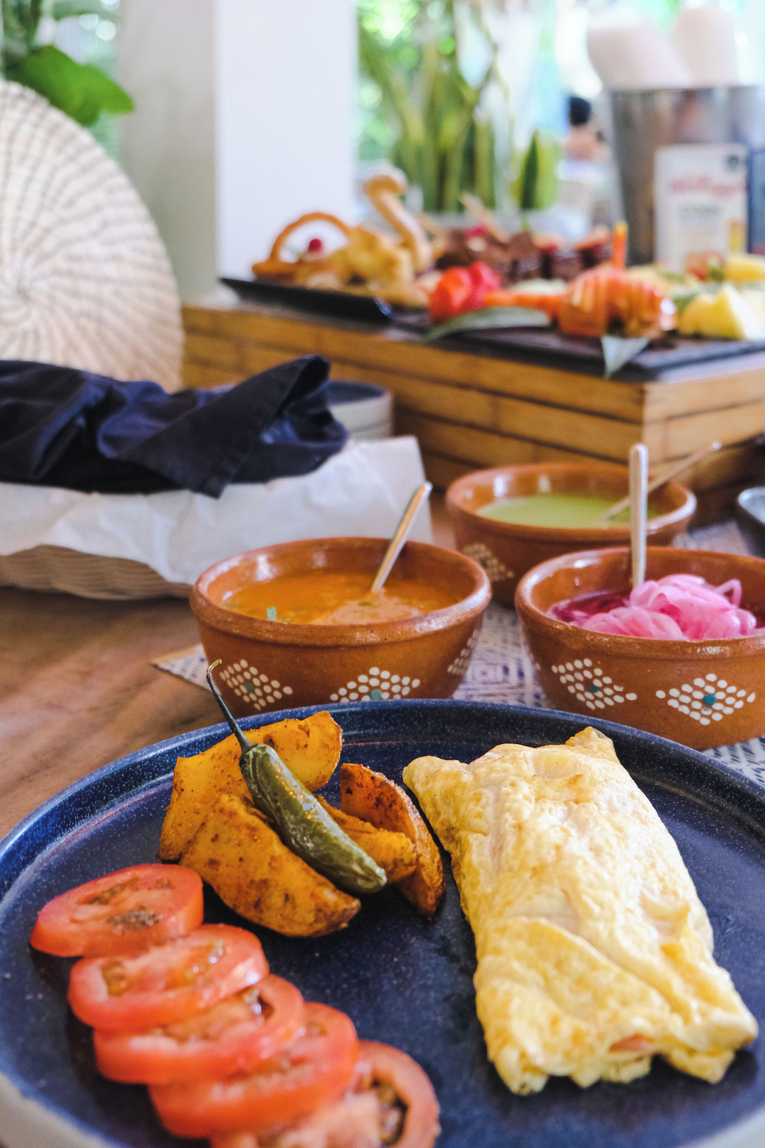 A dining table with a variety of dishes, including a blue plate with sliced tomatoes, a folded omelette, and several bowls with different sauces.