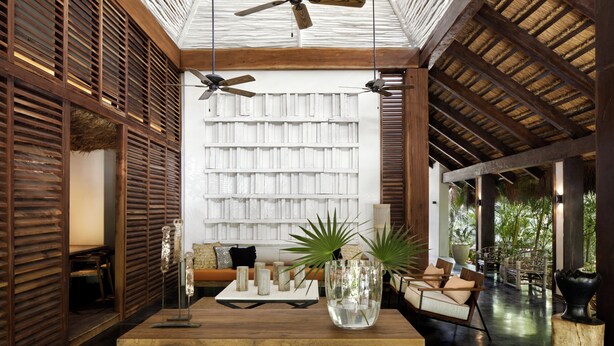 A spacious room with a high ceiling, wooden beams, a large bookshelf, a wooden coffee table, and a seating area with a sofa and chairs. - Aluna Resort Tulum (Tulum)