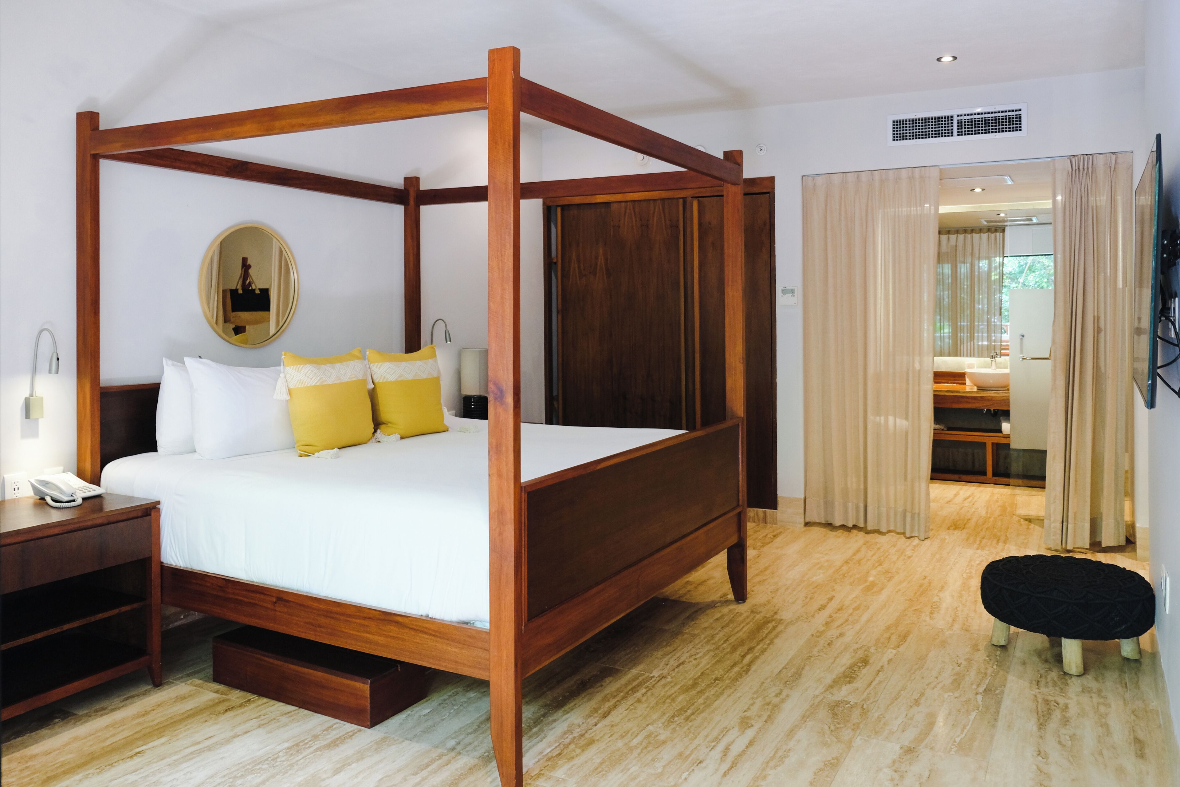 A four-poster bed with a wooden frame, a bedside table with a lamp, and a mirror on the wall.