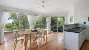 Un comedor amplio con mesa y sillas de madera, una cocina con encimera negra, y ventanas grandes que ofrecen vistas al exterior.