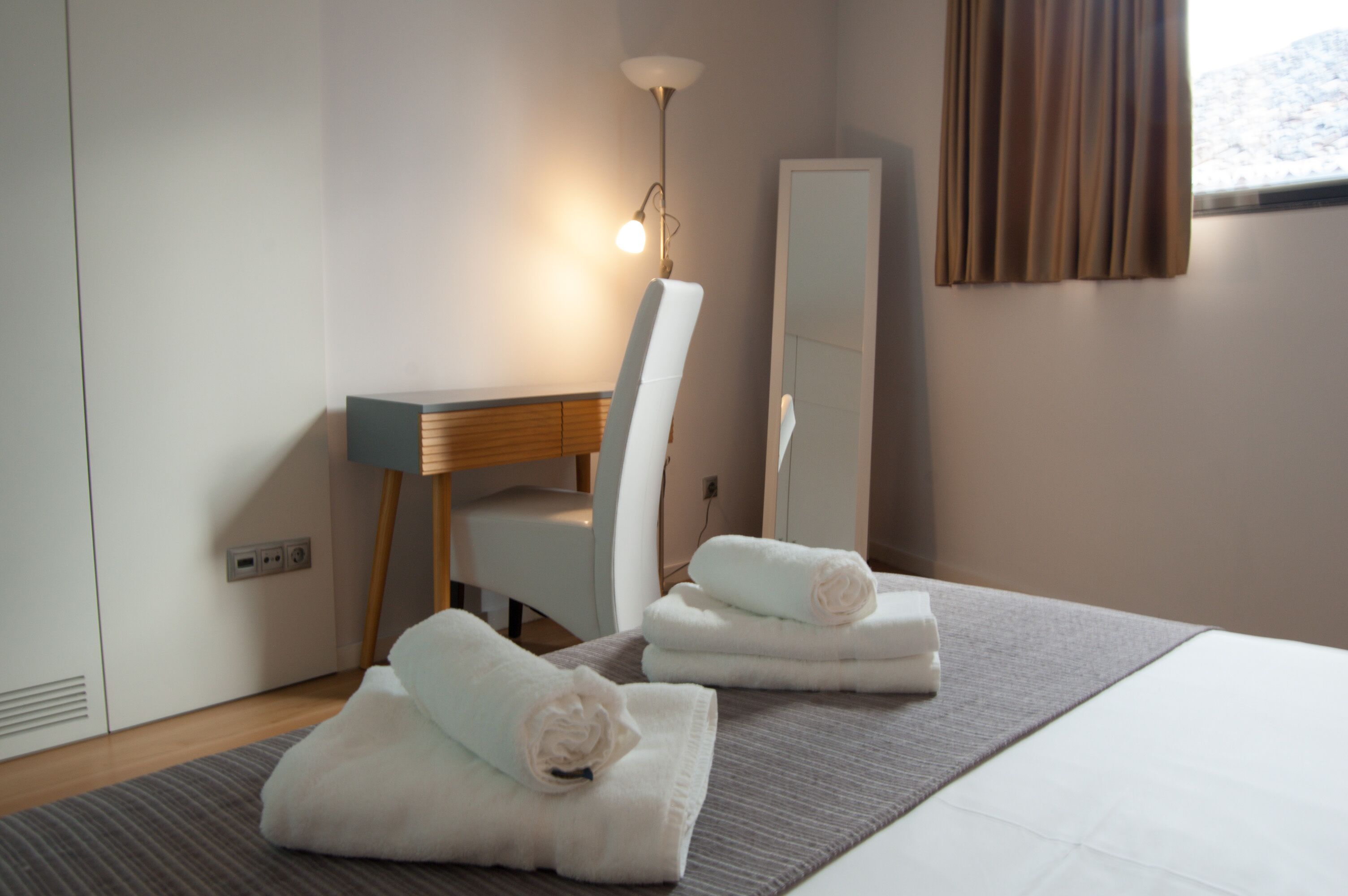 A hotel room with a bed, a desk, a chair, a mirror, and towels.