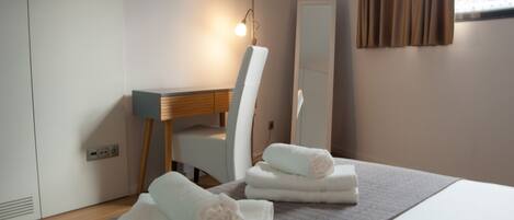 A hotel room with a bed, a desk, a chair, a mirror, and towels.