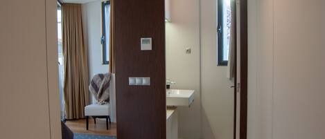 Una habitación de hotel con puerta de madera, una ventana pequeña, un lavamanos blanco y una silla con una manta.