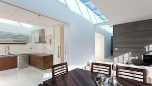 A modern kitchen with a skylight, a dining area with a dark wooden table, and a living area with a sofa and TV. - Atlantic House (Ponta Delgada)