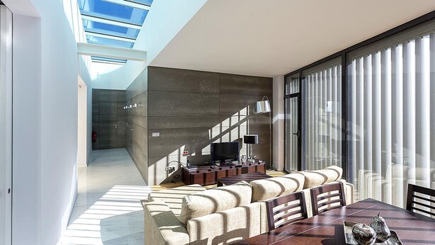 A modern living room with a sofa set, a dining table, and a TV. There is a staircase leading to another level. - Atlantic House (Ponta Delgada)