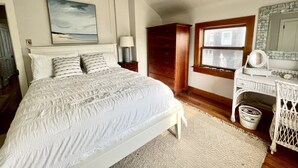 A bedroom with a large bed, a dresser, a nightstand, a window with blinds, and a painting on the wall. - 7br/3.5ba Classic Bay Head Beach House Steps To The Beach  (Bay Head)