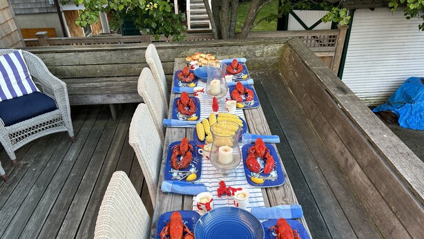 A wooden deck with a long table set for a meal, featuring lobster and corn on the cob. - 7br/3.5ba Classic Bay Head Beach House Steps To The Beach  (Bay Head)
