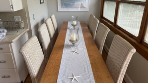 A dining area with a wooden table, wicker chairs, and a view of the outdoors through large windows. - 7br/3.5ba Classic Bay Head Beach House Steps To The Beach  (Bay Head)
