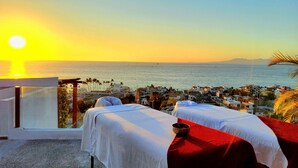 Um quarto com duas mesas de massagem, vista para o mar e uma cidade costeira ao fundo.