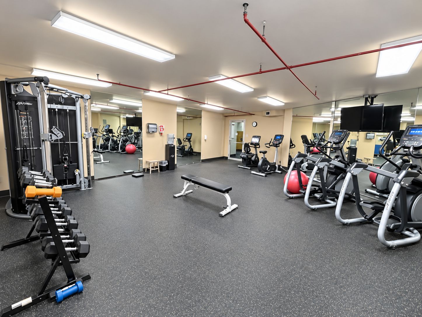 A gym with exercise equipment, a bench, and a mirrored wall.