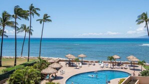 Een zwembadterras van een resort met palmbomen, ligbedden en een helder uitzicht op de oceaan.