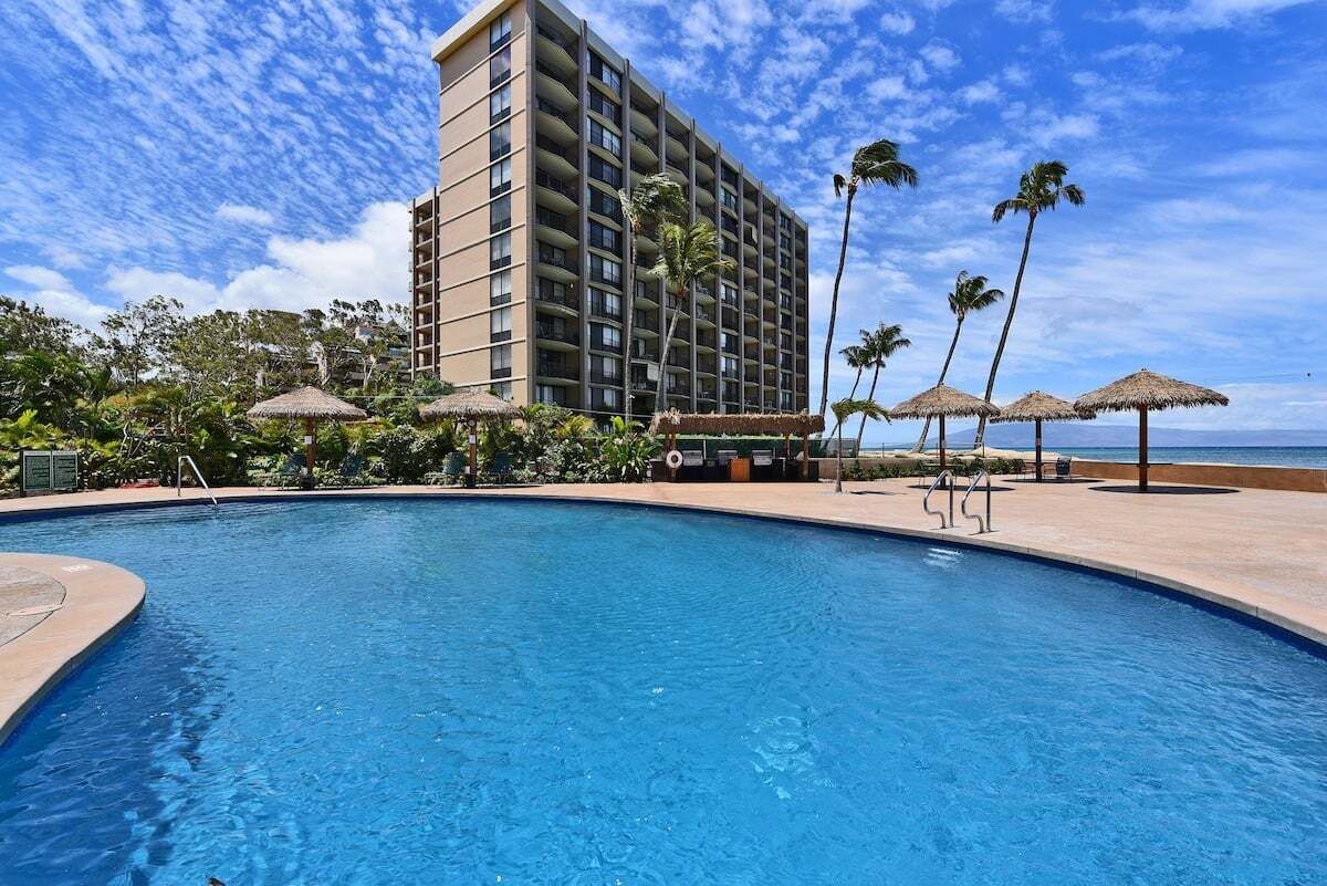 A hotel with a swimming pool, palm trees, and a view of the ocean.