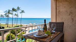 Een eettafel op een balkon met uitzicht op een strand, palmbomen en een zwembad.