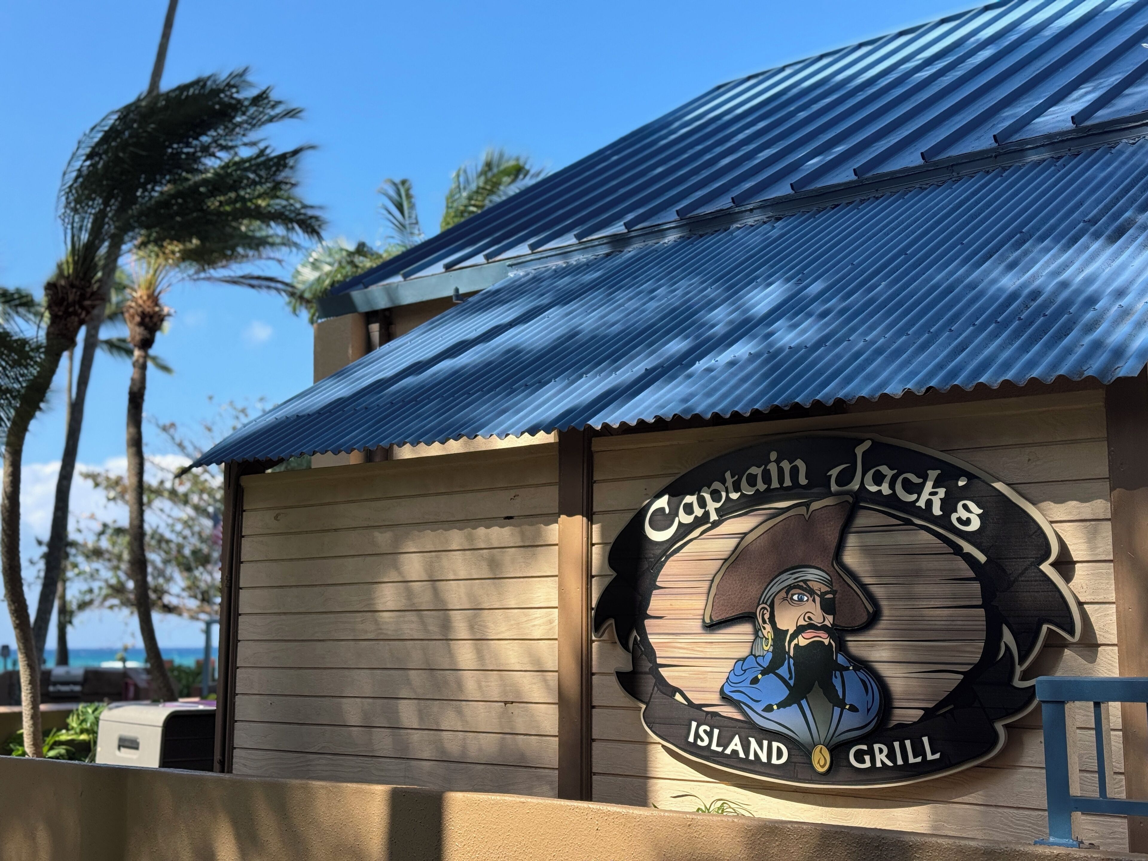 Ein Holzgebäude mit Wellblechdach und einem Schild mit der Aufschrift 'Captain Jack's Island Grill'.