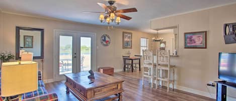 A spacious living room with a wooden floor, a ceiling fan, a television, and a dining area with chairs and a table.