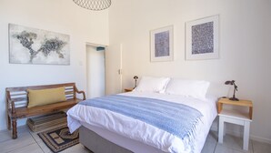 Um quarto com uma cama, um banco de madeira, uma mesa de cabeceira e uma pequena mesa.