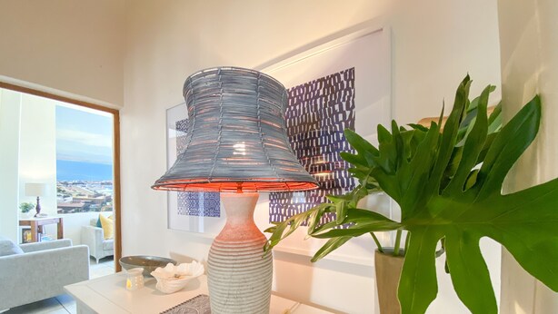 Uma sala de estar moderna com uma janela grande, uma luminária decorativa, uma planta em vaso e uma obra de arte emoldurada na parede.