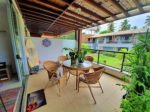 Guests can enjoy a tranquil outdoor space with a round table and wicker chairs surrounded by lush greenery and palm trees.