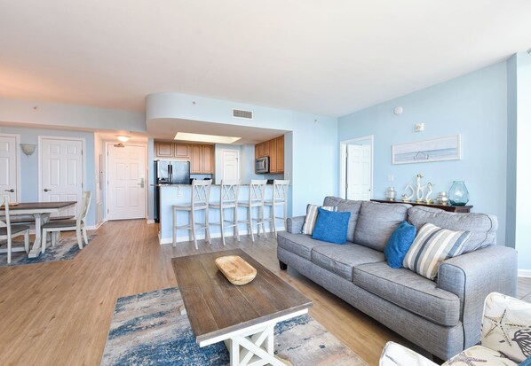 A living room with a grey sofa, wooden coffee table, and a dining area with a wooden table and chairs.