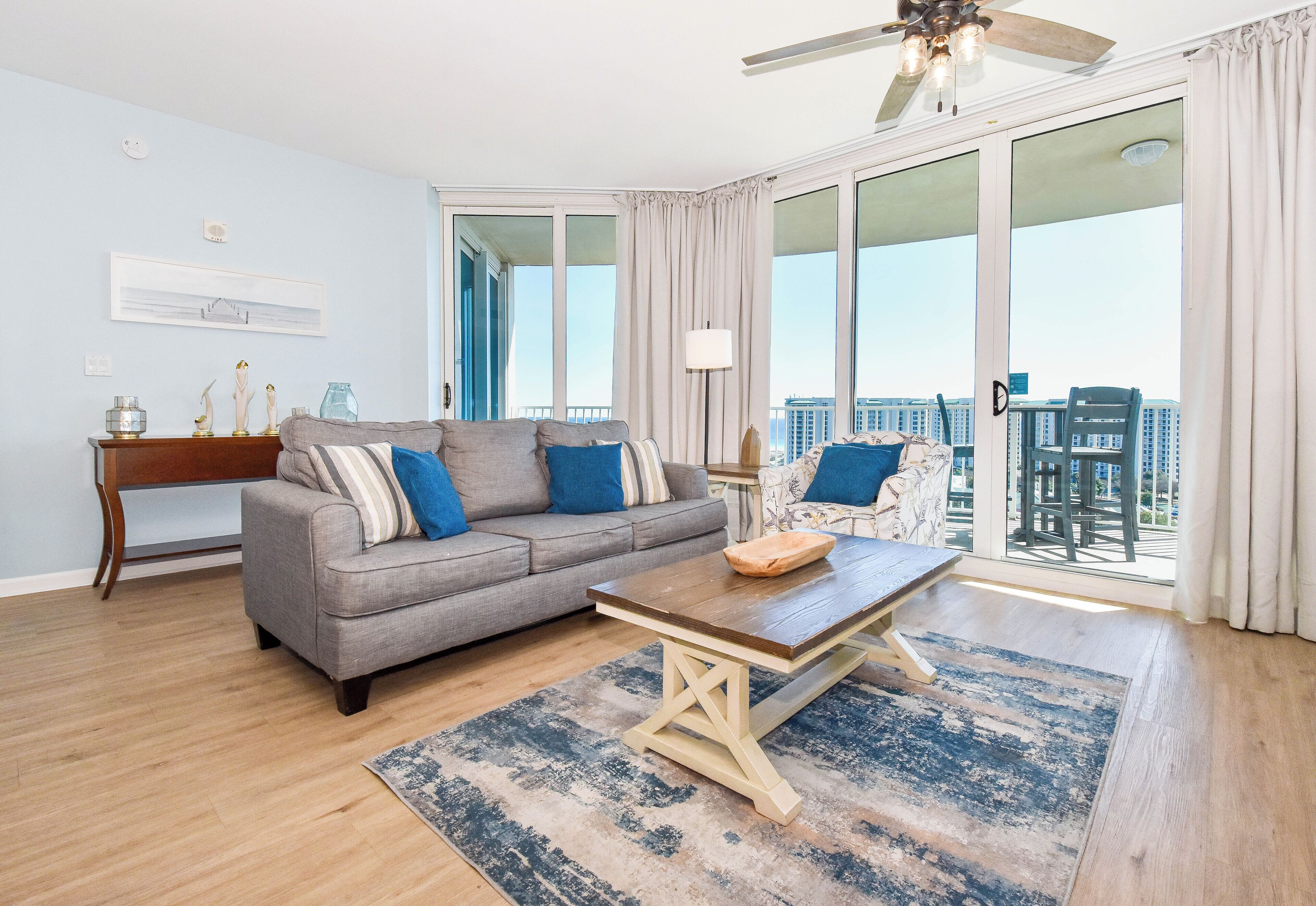 A living room with a gray sofa, a wooden coffee table, and a view of a cityscape through large windows.