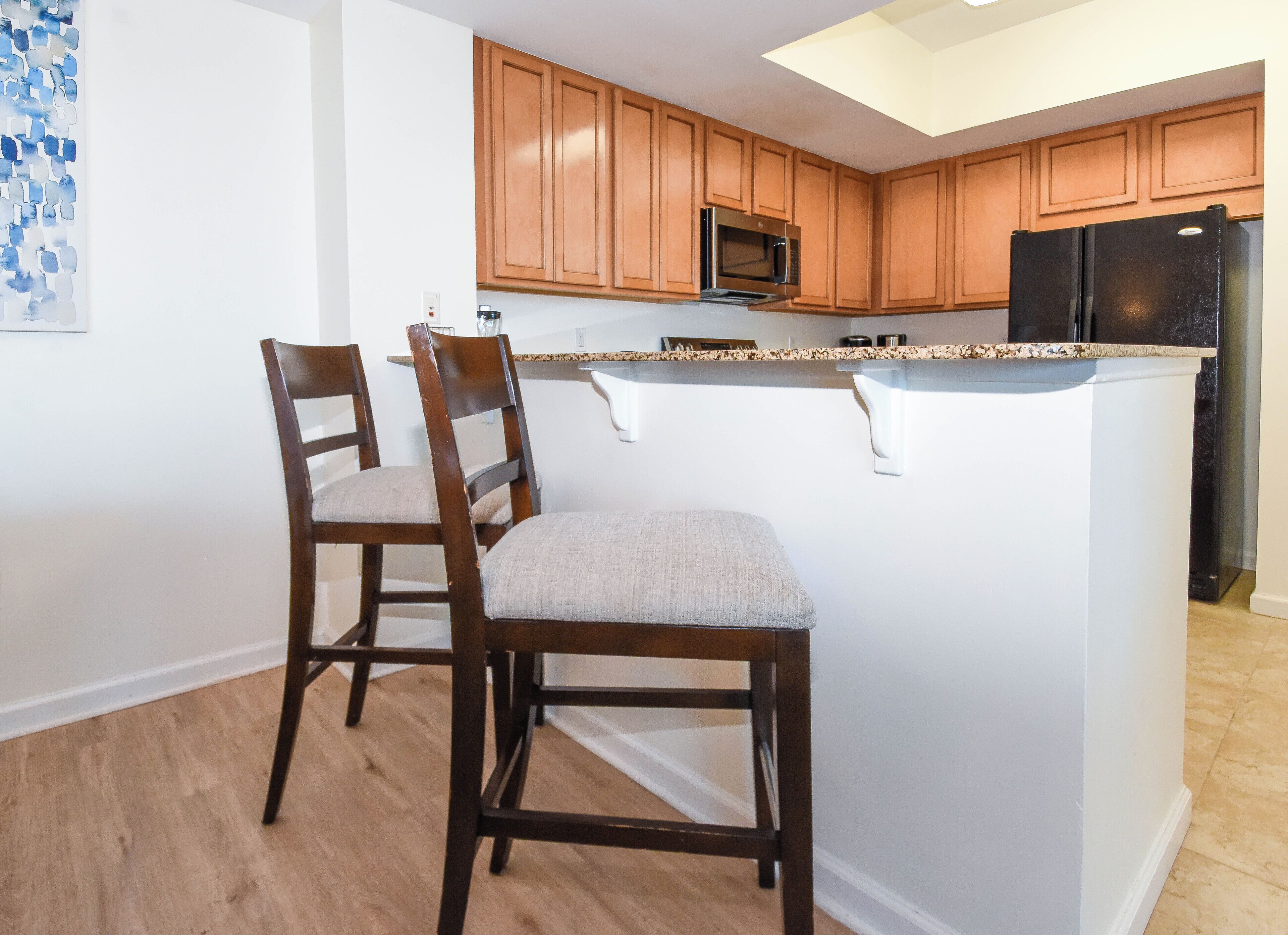 A modern kitchen with wooden cabinets, a granite countertop, and a black refrigerator.